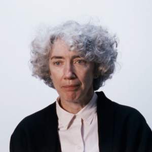 Elizabeth Murray, a white woman with curly silver hair, wears a white buttoned up shirt and black blazer in a white space.