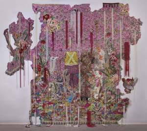 still…. for those who bear/bare witness is an irregularly shaped brocade and sequined installation with 4 partially obscured figures at the center, floral motifs punctuated by strings of beads.
