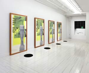 “horror horror” is 4 identical vertical prints in wooden frames, each with a thin Modigliani sculptural bust overlaying a black and white snapshot of a group of white people smiling, a yellow transparent rectangle overlaid, and text reading “The one abo ut the the ee p igs.” In front of each of the frames is a black rubber circle on the floor, and the artwork installed in an all-white gallery space.