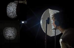 In Cipher is an interactive installation: a person rests their chin on a stand while wearing headphones directly in front of a white open semisphere with irregular light projected onto it.