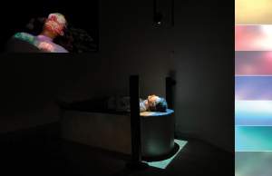 In sensorial experience Into the Dark, a person lays flat on their back wearing goggles and multicolored lights are projected onto their face in a darkened room.
