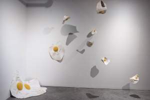 Macroverse is an installation in a gallery space, with various mini quilts styled as fried eggs suspended from the ceiling
