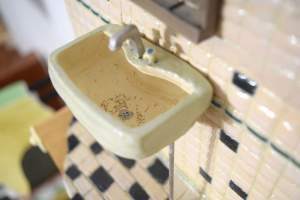 In this detail of I Can Hear Your Dirt is a miniature bathroom sink mounted on a tile wall with hairs in the bowl.