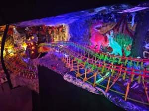 This detail of The Haunted Hearse Phone Rollercoaster shows a miniature fluorescent rollercoaster surrounded by quilted background scenes, faux fur textures and other scenery, including dinosaurs, skeletons and a haunted house.
