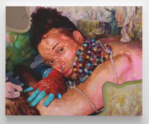 A person with curly hair reclines on a surface, wearing multi-colored beads, a red textured glove, and blue gloves, with a neutral expression and a textured, abstract background.