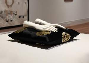 In the Mud, What is More Beautiful Than a Lotus? Is a sculpture composed of two white porcelain hands with long square shape nails on a black silk pillow with gold medallions.