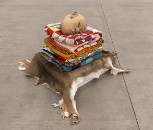 A stack of colorful folded quilts topped with a ceramic head rests on an animal hide laid on the floor.