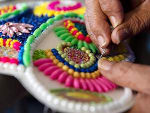 Sew, Sew, Sew is a photo showing detail of hands sewing beads of many colors and shapes onto a medallion in a concentric pattern.