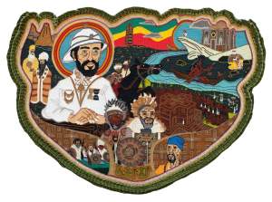 “Ethiopia” is a large beaded apron medallion centered on a depiction of Haile Selassie, the former Emperor of Ethiopia in white military suit with folded hands and a white pith helmet. He is surrounded by other motifs including Nyabinghi warriors, a rock-hewn church in Lalibela, Ethiopian hermit monks, and the Obelisk of Axum. The apron is bordered in a velvet green ruffle.