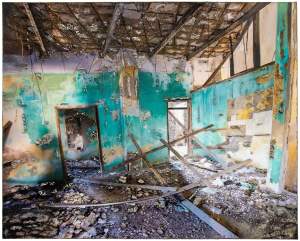 “Bends of Wood Grid (Turquoise Room)” is an rectangular altered photograph of a dilapidated interior in space in Haifa, Israel. The room has two door openings, and an angled ceiling with wooden beams. Debris covers the floor, and wood scaffolding has collapsed. The heavily distressed walls are turquoise, yellow and white, and the photograph is marked all over with textured cement pushed through areas of the photograph.