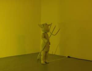 It's atavism is a sculpture of a potentially life-size figure of Hot Stuff the Little Devil standing alone in a corner, illuminated by amber fog lights mounted on the opposite wall.