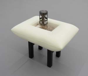 The cat in my brain is walking is a sculpture of a sleeping cat sealed in a pillowed vitrine. The table-like structure holds a single cast porcelain oil lamp, lit beneath an ornately cut metal can.