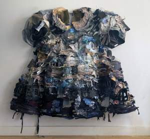 In The City Of Children is a sculptural textile work hung on the wall, in which many scraps and pieces of layered fabric form a larger-than-life child’s dress. On the surface of the dress, forms of houses and windows are visible.