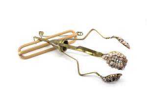 Body Weaponized No. 8 is a sculptural object resembling a tool of uncertain purpose. 4 radial arms of bent metal extend from a center cup, each with a mesh spoon covered with enameled disc beads.