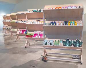 Future Fossils: No Nouns Left Whole is an installation of 6 rolling angled shelf displays, each holding rows of colorful bisected mass-produced plastic containers, some in the shape of bottles, other in the shapes of fruits and plants.