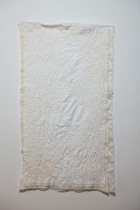 Microverse is an off-white irregular rectangular quilt hung on white wall, with hundreds of circles with yellow dots like small fried eggs embroidered in clusters.