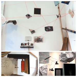 Art installation featuring red strings connecting various objects and images on a white wall. Items include photographs, papers, and stones, with a focus on connectivity and tension.