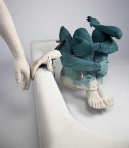 Bottom of The Shower is a sculpture of a fragmented incomplete blue figure with 3 arms wrapped around knees, and another reaching out to touch edge of a shower edge. Another disembodied white hand reaches down to graze the fingers.