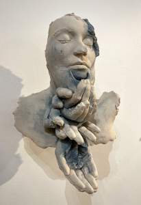 Grieve is a sculpture of a face with closed eyes, and a stack of four cupped hands below the chin.