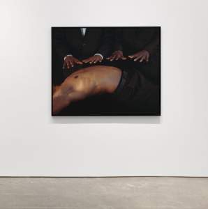 A painting on a white wall depicting two people in suits resting their hands on the back of a shirtless person.