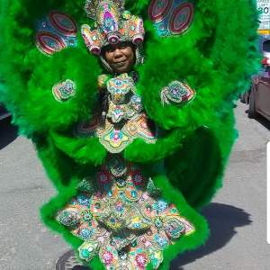 Denise Smith wears an elaborate green feathered suit with beadwork depicting lush foliage and natural motifs.