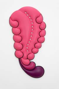 This sculptural piece, called Closer, hangs on a wall. A carnation-pink, tongue-like form swells upward and is flanked along both sides by comma shapes. Three Two longer swirls curl out from the bottom in darker pink and purple. The upholstered piece has a line of fourteen round-headed pearl nails.