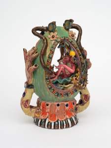 Garden Egg is a surreal ceramic sculpture by Los Angeles-based ceramic with the figure of the Pink Panther seated inside a floral, oval frame with surrounding hands, tentacles, and intricate, colorful designs on a green and orange base.