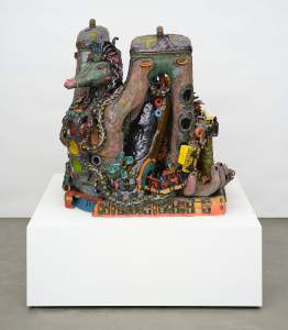 Weighing of the Heart (angel of LA) is a colorful sculpture with various textures, jewels, and small objects integrated into a dragon-like fantastical creature on a white pedestal display.