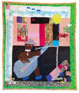 B.B. King Concert In The Garden is a colorful quilt featuring a man playing guitar, animals, abstract shapes, and various patterns. An American flag is in the top left corner. The quilt has a green floral-patterned border.