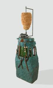 Untitled (shawarma topiary) is a mixed media sculpture, resembling a vertical rotisserie with a cone-shaped meat stack on a rotating mechanical spit on top of a textured, teal base with multiple brown leather straps.