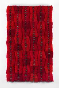Proximate Parcels is a rectangular vertical textile artwork featuring vertical rows of mixed tones of red textured threads with small dark circular accents arranged in vertical, spine-like evenly spaced lines.