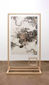 A gray, black, and golden-brown drawing on white paper is displayed between sheets of clear acrylic in a wood floor stand. The drawing shows nests and tangles of snakes, and a papery snakeskin kinks wildly in a smaller box inset near the lower right corner.