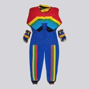 This beaded fire suit has a high collar, long sleeves and pants, all with fitted cuffs, and a pair of partially beaded gloves. The suit zips up the front and is laid flat with the arms folded over the torso. The shoulders and chest are horizontally striped and the pant legs vertically striped, all in shades of vivid red, yellow, green, light blue, and jewel-toned lapis blue.