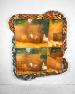 A blurry photo with a cloud of dirt kicking up from an almost unseen car is partially repeated four times across an almost square rectangle, which is edged unevenly with braided tubes of cloth. Smaller versions of the image create lighter or darker fields in the overall grid.