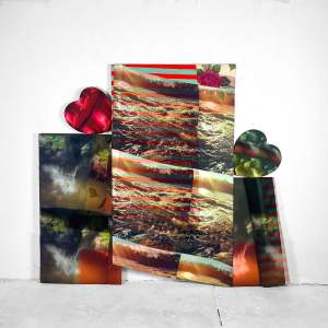 Layered images printed on cloth overlap to create three main panels, with the central panel being taller than the flanking strips. Hearts, one ruby red and one mossy green, rock onto their sides atop the side panels to either side. Imagery across the work includes waterfalls, churning water, red and turquoise stripes, and a floral pattern.