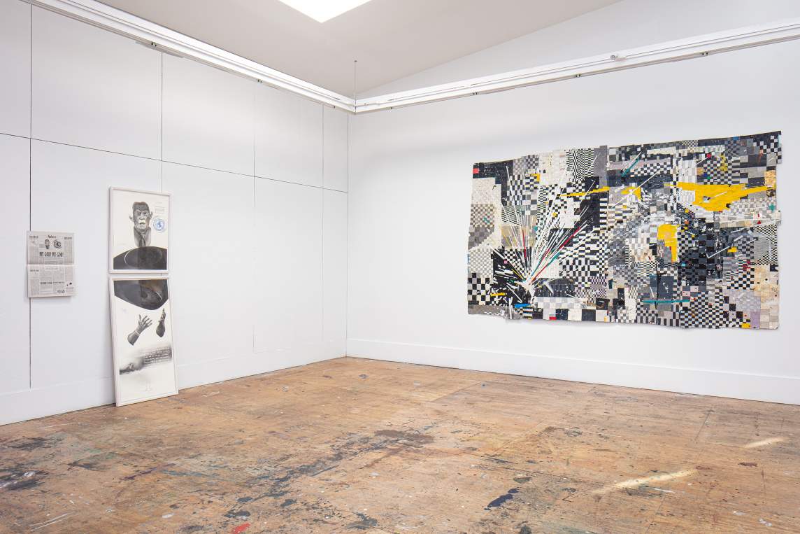 In an art studio with white walls and distressed plywood floors, a drawing in two parts rests on the left wall, with a newspaper hung next to it. The drawings depict the face and hands of a man, with an abstract shape in between. On the right wall, a large collaged artwork hangs. Predominantly black and white, it has dynamic radiating lines and checkerboard patterns.
