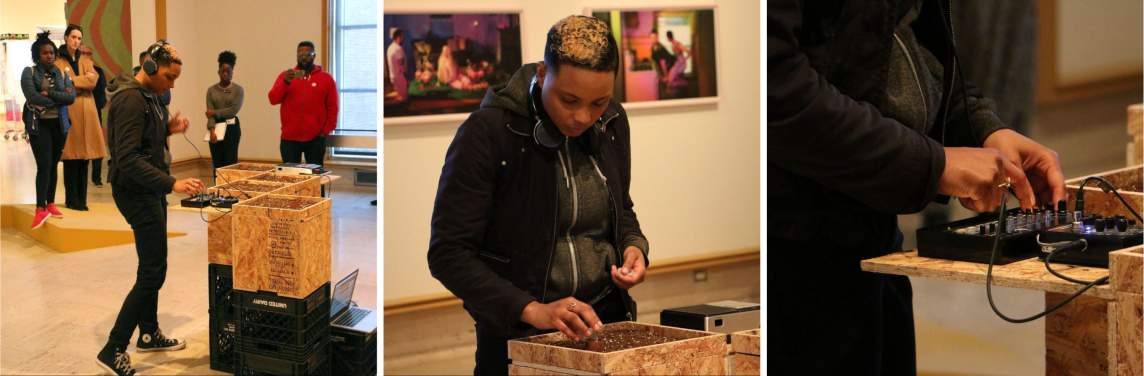 A composite image of artist Ash Arder, a person with dark skin tone and short dark hair with a blonde streak, activating her project Broadcast #3 in a gallery space with visitors present. The sculpture is made of plywood boxes, filled with soil and fitted with electronic parts that operate speakers inside the boxes.