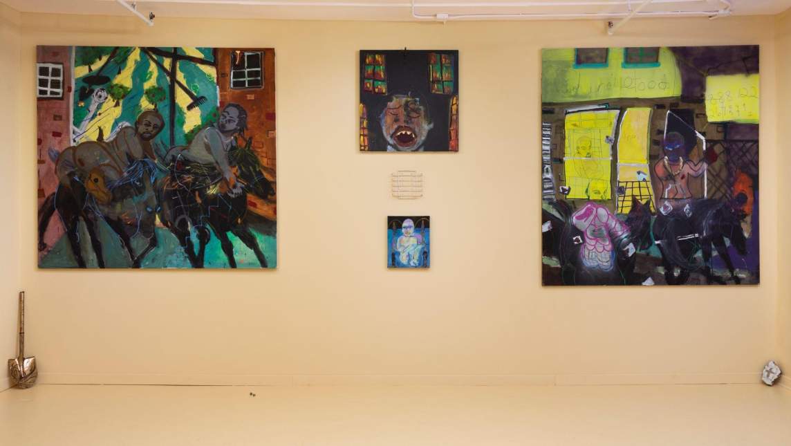 On a white wall two large almost square paintings flank 3 smaller pieces hung in the center, with a small metal shovel leaning against the wall on the far left. In the left painting, two gray-brown figures ride black horses, with brick buildings and a striped field in the background. In the right painting, in front of a yellow window and an awning reading “Chinese Food", a shirtless figure with a mask-like purple face rides a dark horse, and to their left is a figure with pink outlined muscled torso and transparent head indicated with light lines.