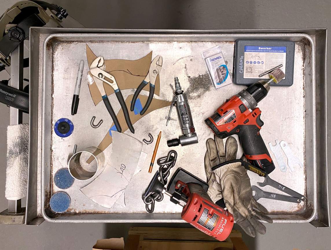An overhead shot of tools on a metal tray in the studio of Peggy Chiang. We see wrenches, Dremel tools, gloves, and bits paper.