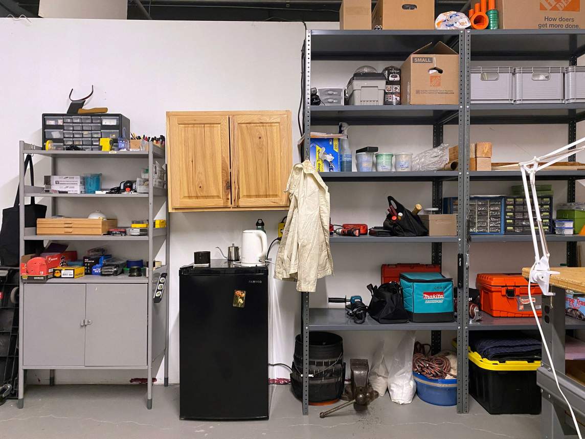 A wall in an artist's studio with shelving and cabinets holding various tools and materials.