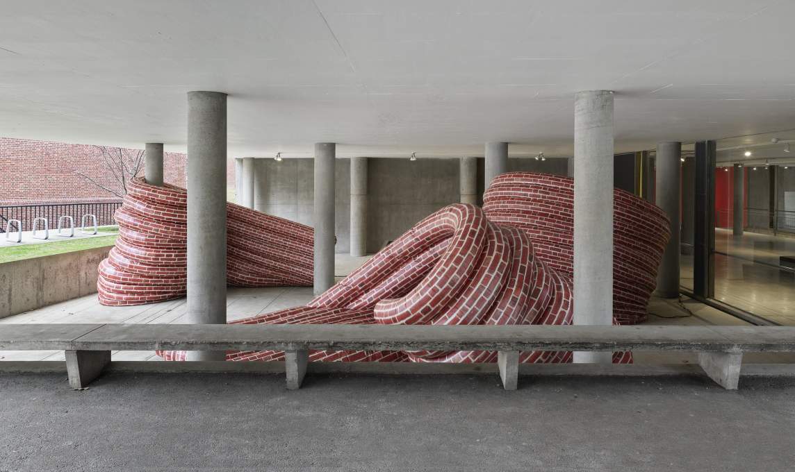 Art installation featuring large red and white striped fabric pieces draped over concrete structures, creating dynamic shapes within a stark, modern architectural space.
