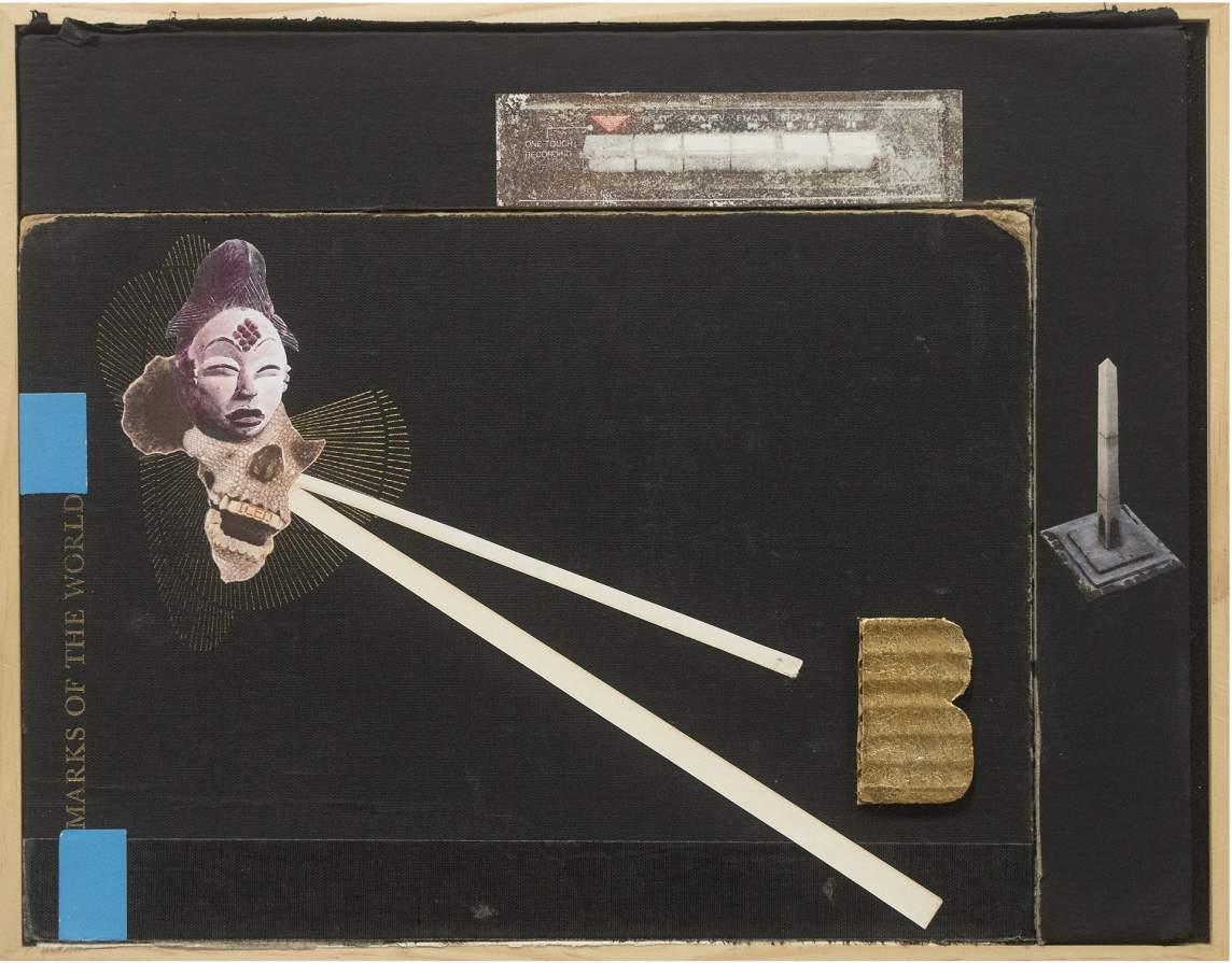 In a detail of a sculptural assemblage, a black book titled "Marks of the World" is inset sideways into a black panel in a wooden frame. Mixed media elements are applied to the surface assemblage-style, including cutout photos of an Asian mask, a skeleton, and an obelisk, a cardboard cutout of the letter B with no holes in the letter, and diagonal white lines and blue rectangles.