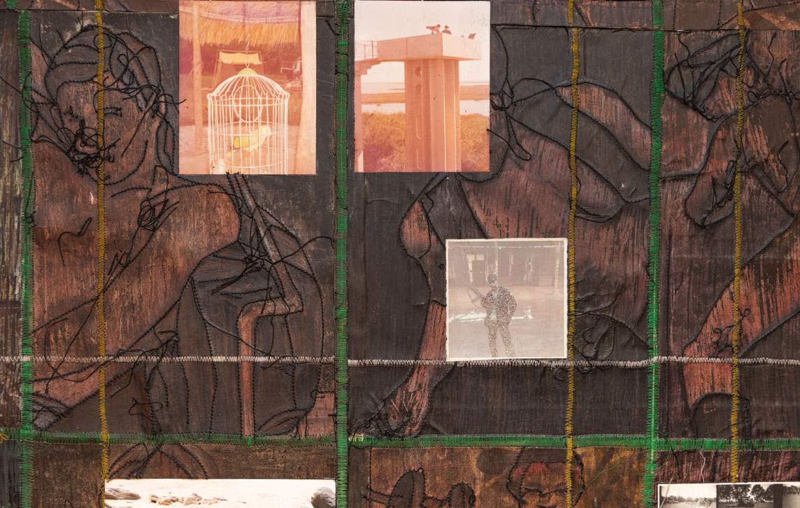 Red-tinged photographs of a bird in a cage and people atop an observation tower along with a photograph of a soldier bracing a long gun against his side are set against a dark brown background. The outlines of people are stitched in black on the background, and lines of white, green, or yellow slice across the surface.