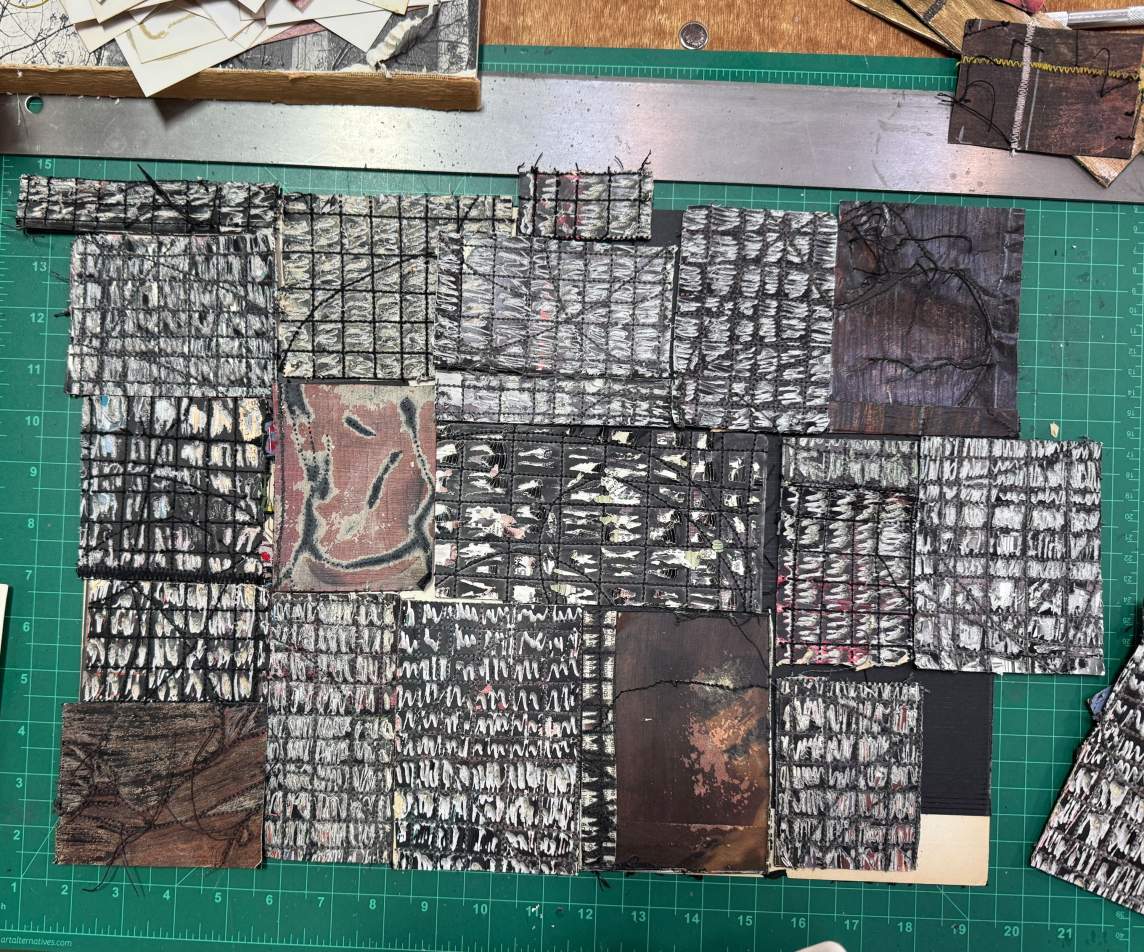 We look down onto a self-healing cutting board laid out with a patchwork of squares and rectangles. Most are black with white hatching or dashes, and a few are mottled shades of dark brown.
