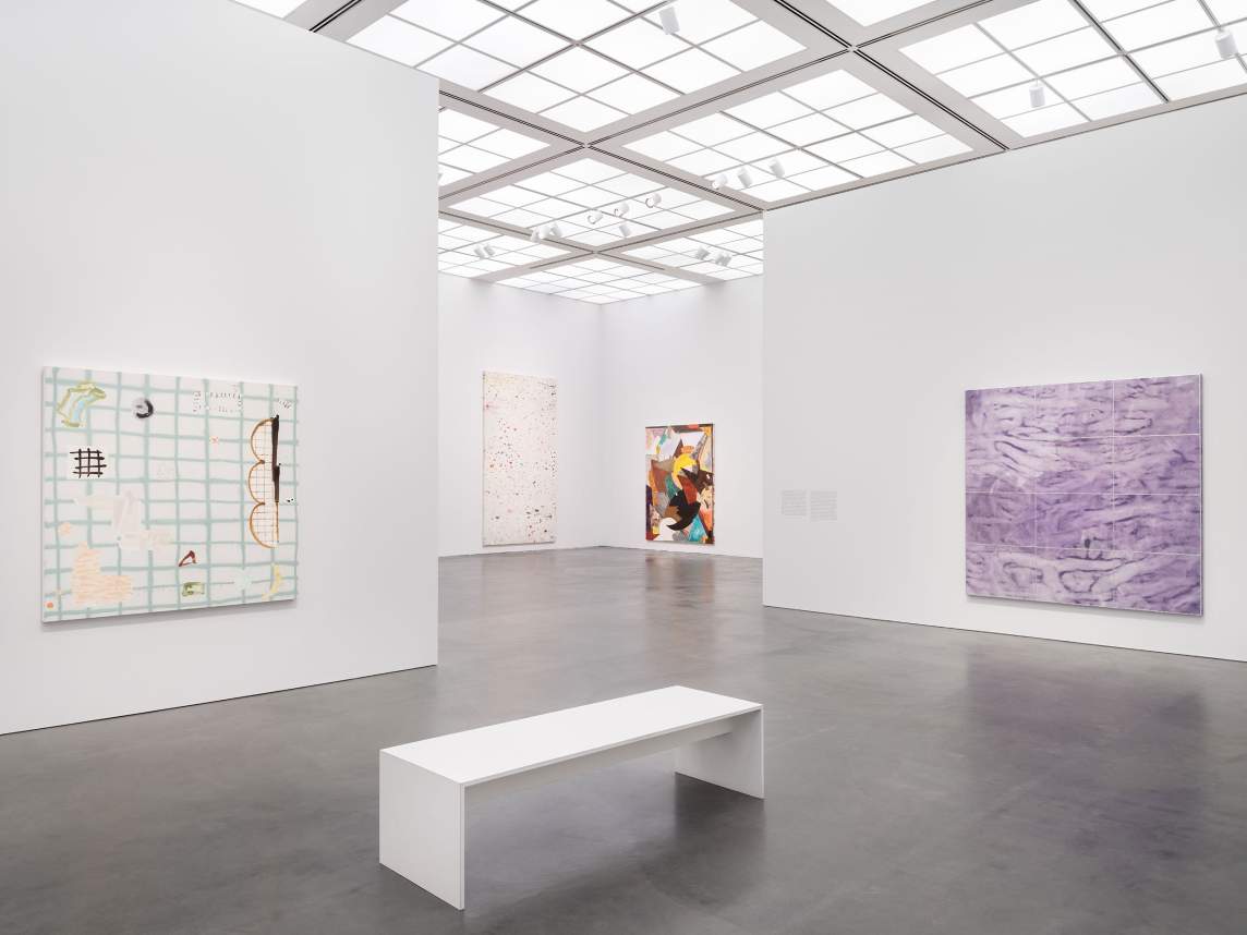 Four abstract artworks hang in airy museum gallery with white walls, glass ceilings, concrete floors, and a white bench.