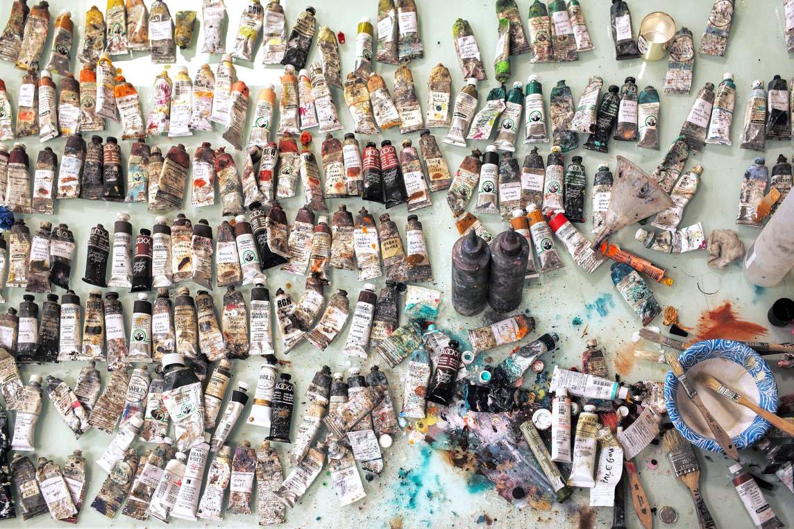 Dozens of paint tubes lay on a studio work table.