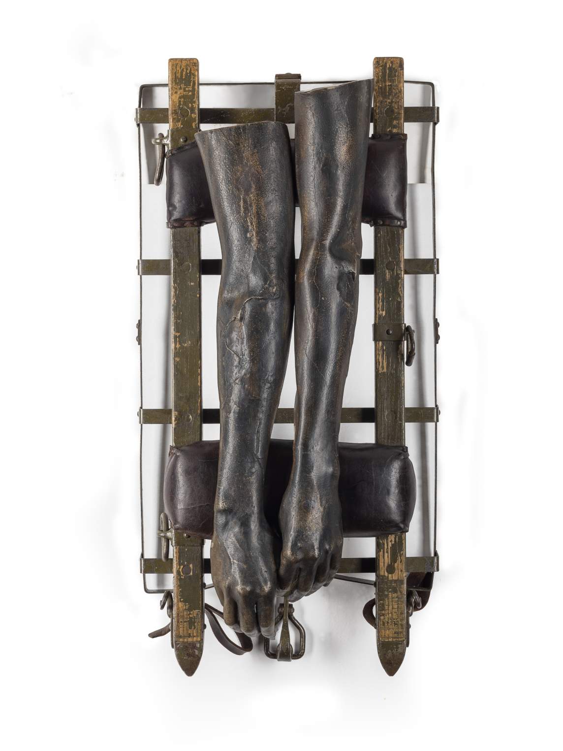 This sculpture is made up of two human arms from fingertips nearly to shoulders cast in bronze. They lie relaxed, hands hanging down and across leather pads along a grid of narrow wood planks and metal strips.