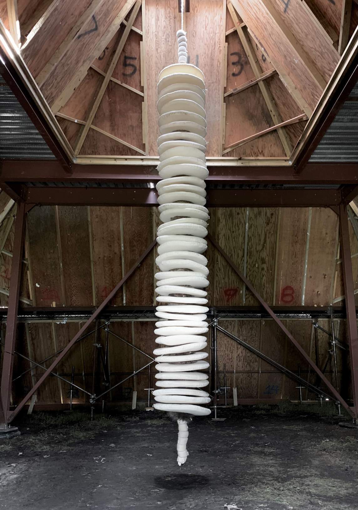 Forty flat, slightly irregular white disks are strung up a thick white rope, which hangs from the peaked ceiling of a two-story opening.