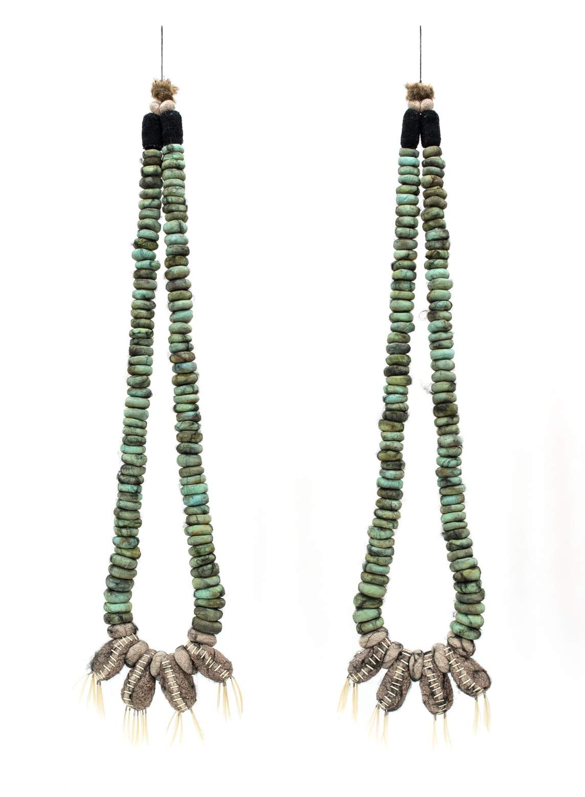 Two strands strung with ocean-green, flat, round beads hang side by side. The ends meet in black caps under fuzzy tan tufts at the top. At the bottom center of each are four light gray, clam-like shapes made from fiber. The seams around the edges are stitched in white, and yellow strands hang down from the bottoms.