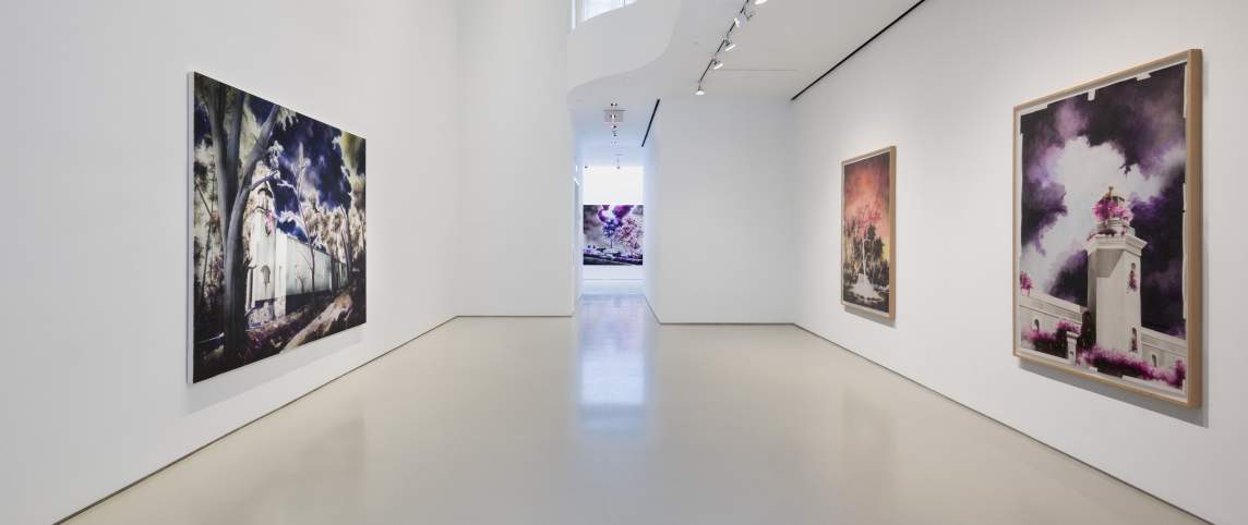 Art gallery interior with large landscape paintings on white walls and a polished floor.